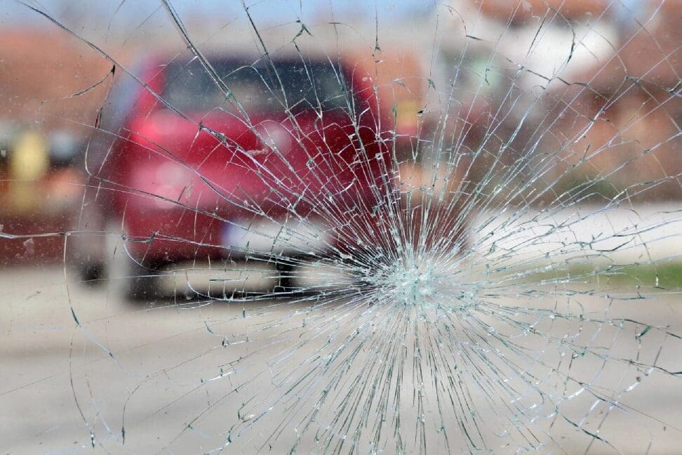 Red blurred vehicle seen through a spider-cracked glass needing windshield replacement.